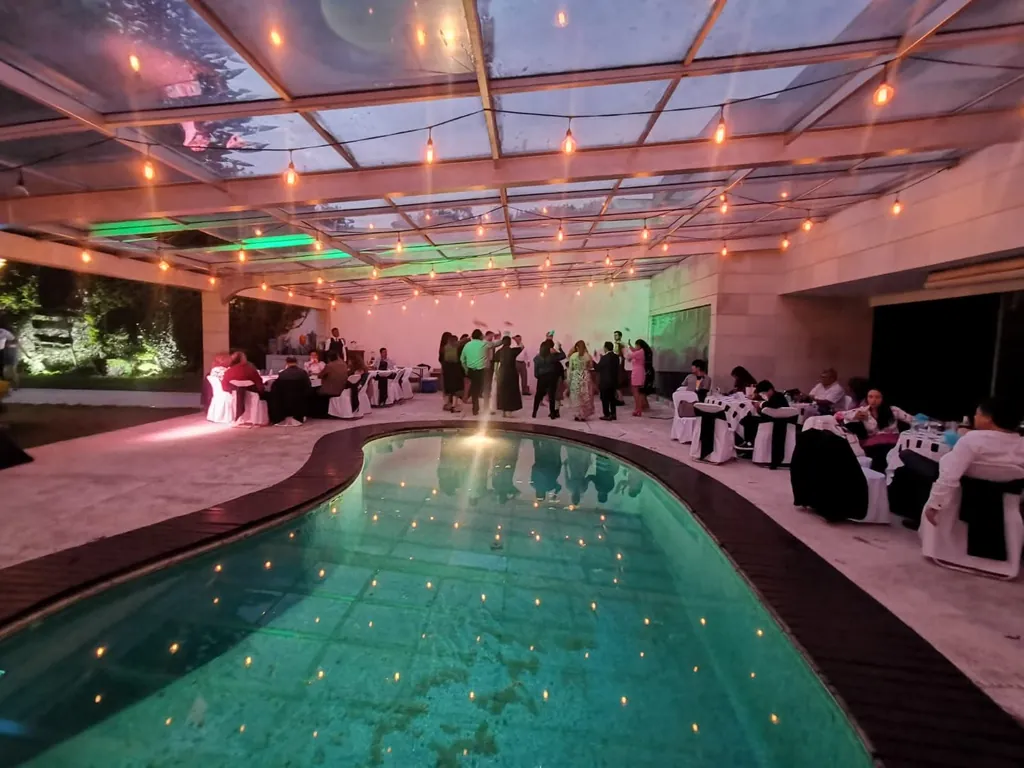 Alberca techada del Jardín Coyoacán de noche, con series de luces cálidas y un evento en curso