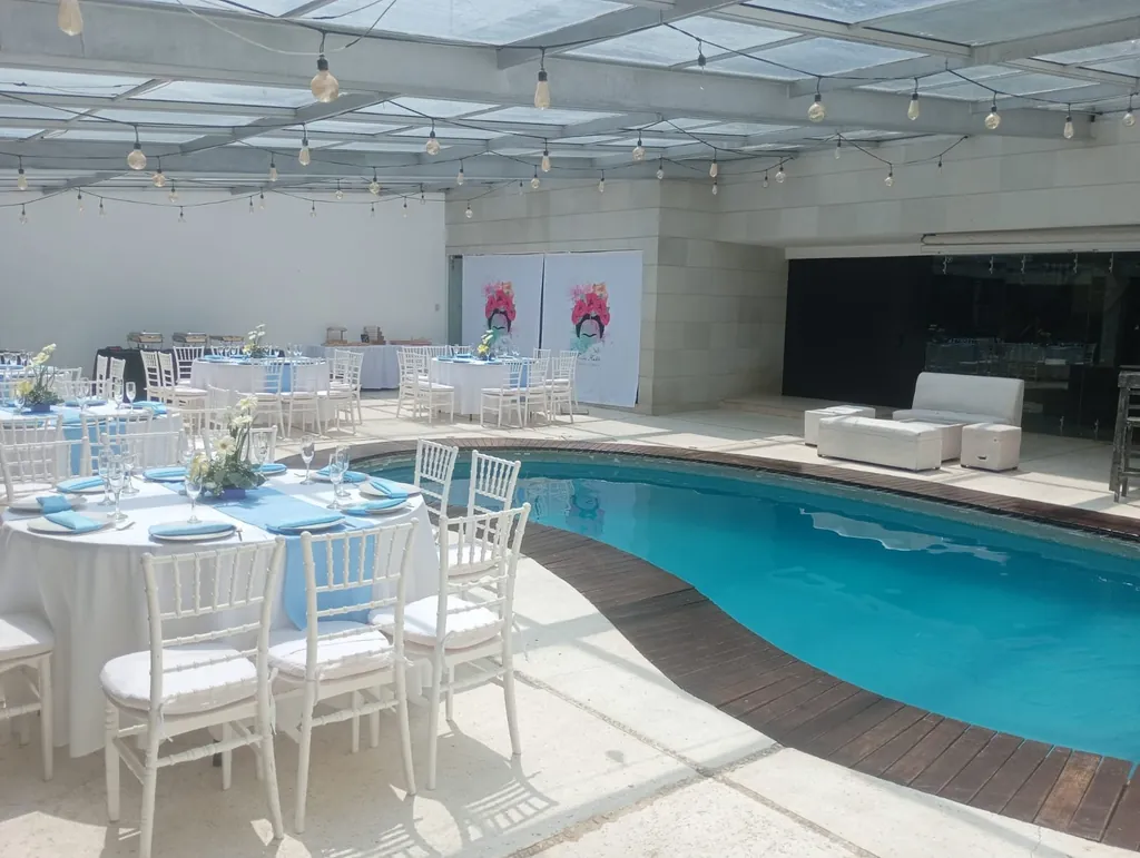 Montaje claro de día junto a la alberca, con mesas redondas, sillas blancas y una sala lounge